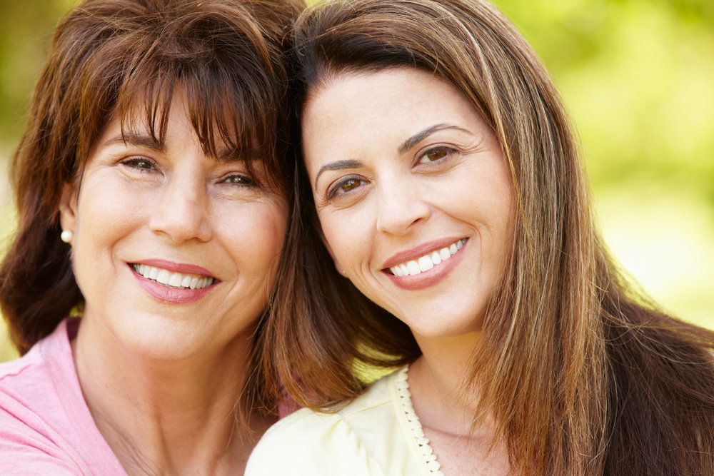 Two brunette women smile after having dental bridges placed